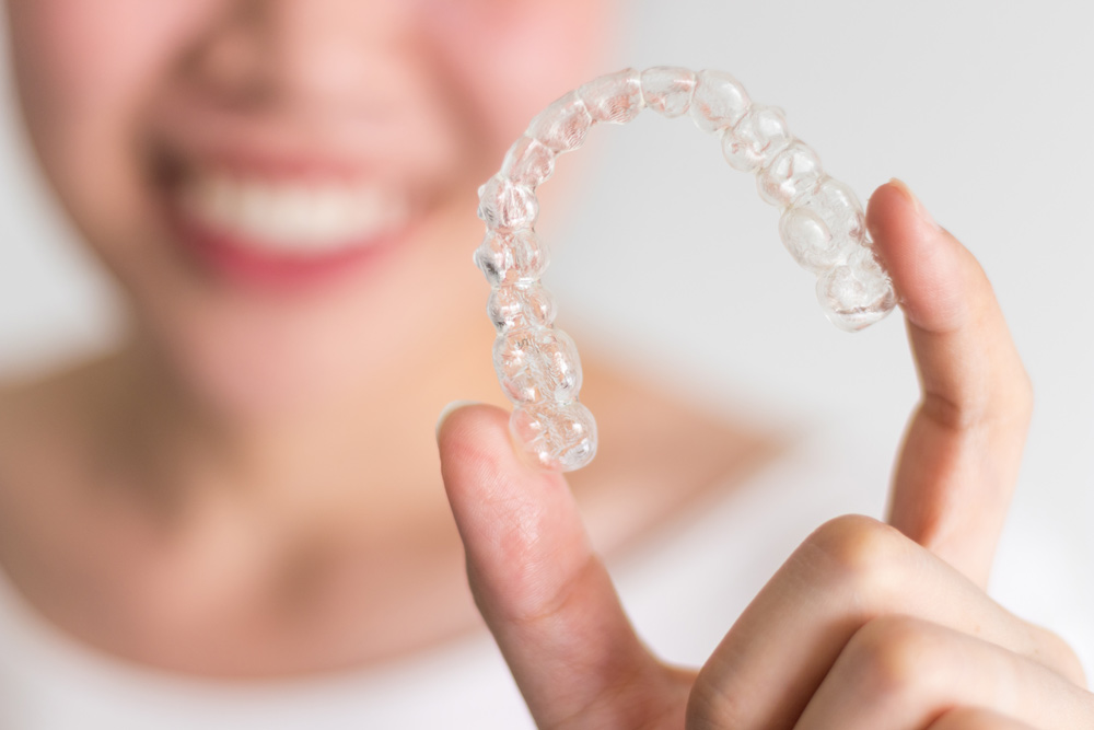 A smiling woman holding invisalign or invisible braces, orthodon